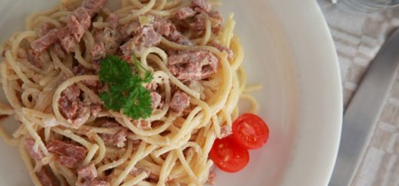 Vit tallrik med pasta carbonara sedd ovanifrån, till höger på tallriken en halverad cocktailtomat 