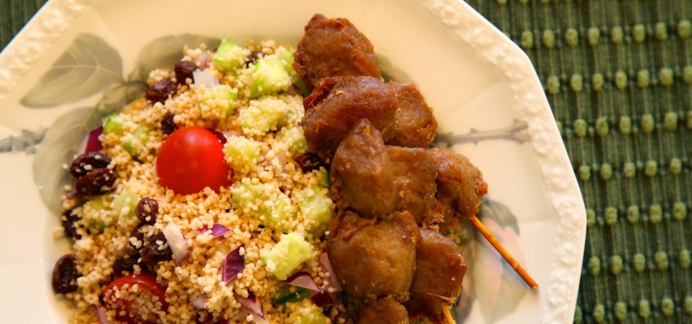 Couscoussallad med tzayspett till höger på vit åttakantig tallrik sedd ovanifrån, står på grön textiltablett.