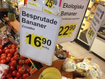 Bild på butiksskyltning av bananer, en skylt anger "Besprutade Bananer" den andra "Ekologiska Bananer" samt prisuppgift.