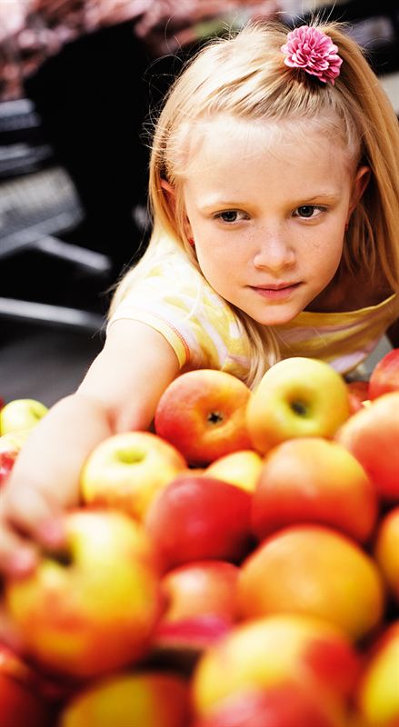 En flicka vid en fruktdisk full med rödgula äpplen sträcker ut handen för att ta ett äpple