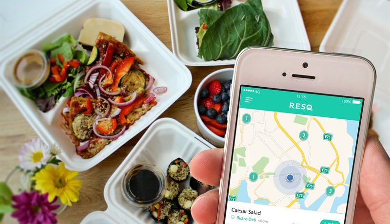 Smartphone med appen ResQclub uppe, i bakgrunden vita fat med bär och grönsaker.