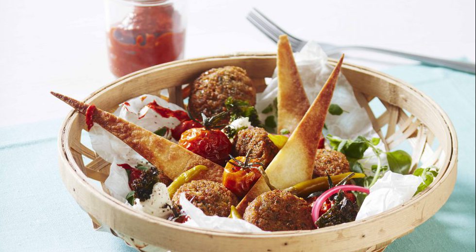 Maträtt med falafel i en korg på bord med vit du och mintgrön bordstablett.