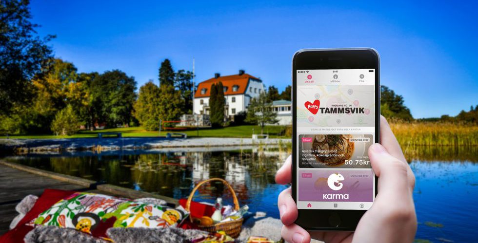 Smartphone med Karmaappen öppen, i bakgrunden en sjö och ett vitt större hus, en konferensanläggning