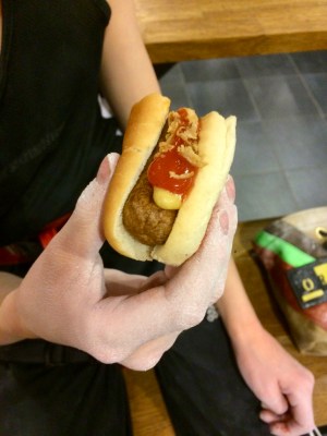 Barnhand håller i en halvt uppäten varmkov med bröd, senap, ketchup och rostad lök.