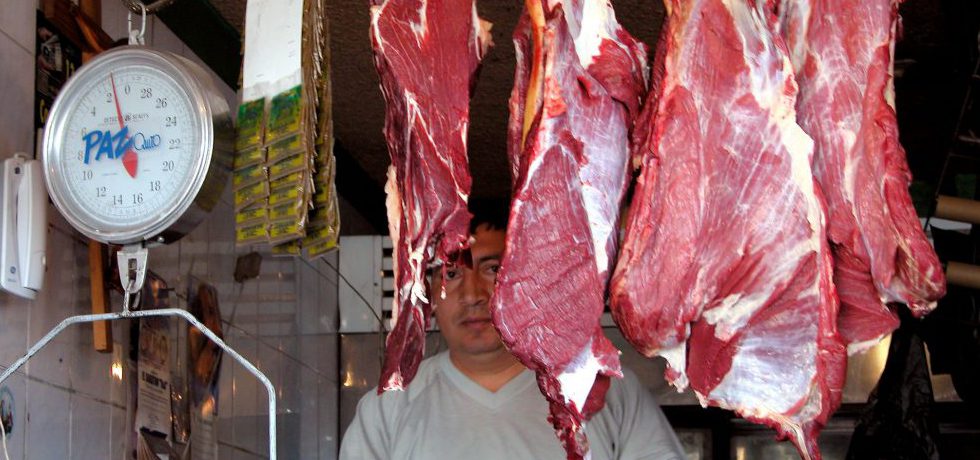 En man står bakom styckade, upphängda köttdelar