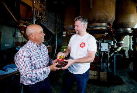 Två män där de ler mot varandra och överlämnar ett paket kaffe