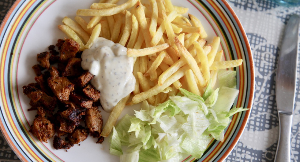 En tallrik sedd uppifrån med kebab, pommes, isbergssallat och i mitten en vit sås