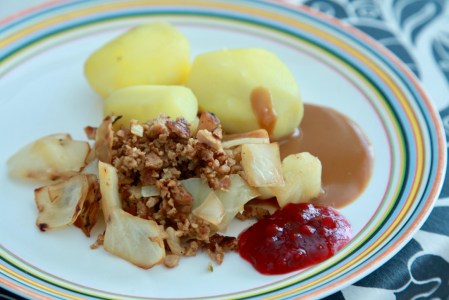 Kålpudding med kokt potatis, brunsås och lingon på en tallrik med ränder längst ut