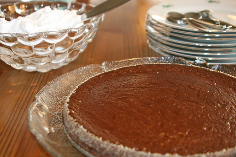Kladdkaka på glasfat, vispad grädde och assietter i bakgrunden