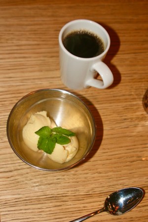 Metallskål med två kulor sorbet i gul ton samt en vit kopp med kaffe