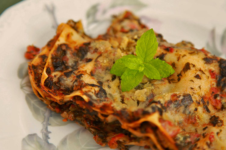 En rektangulär bit lasagne, toppad med mynta på en tallrik