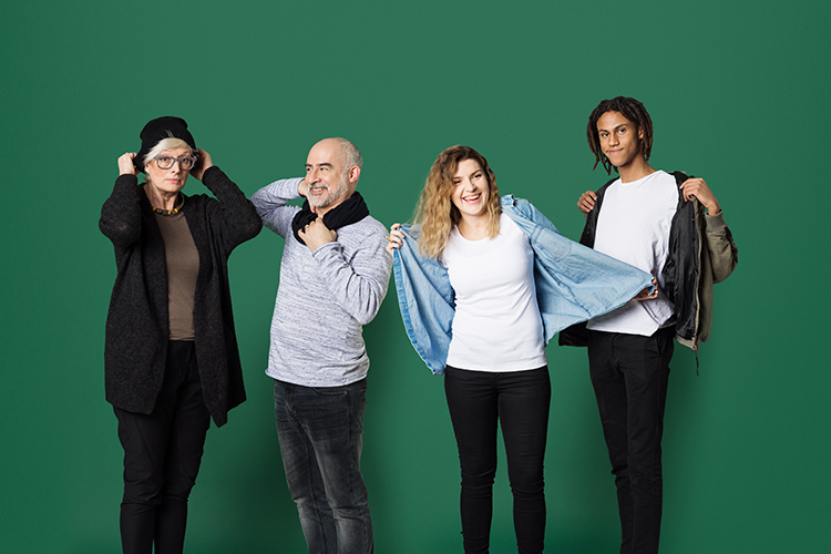 Fyra personer mot en grön vägg som tar på sig en skjorta, mössa och halsduk