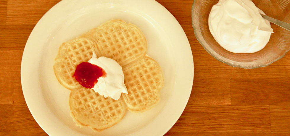 Våffla med sylt och grädde på, till vänster grädde i en glasskål