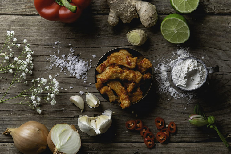 Lök, vitlök, ingefära på ett bord, i mitten en skål med kycklingliknande bitar, Veg Chili Giingerstrips
