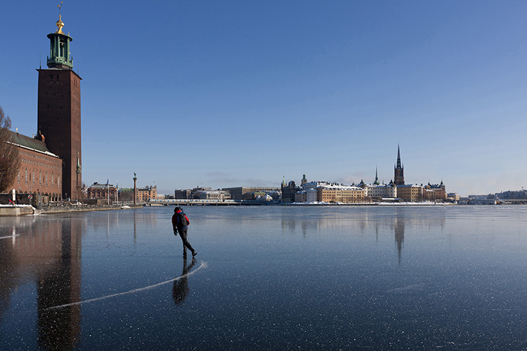 En skridskoåkare på blank is på Riddarfjärden i Stockholm, till vänster syns Stockholms Stadshus.