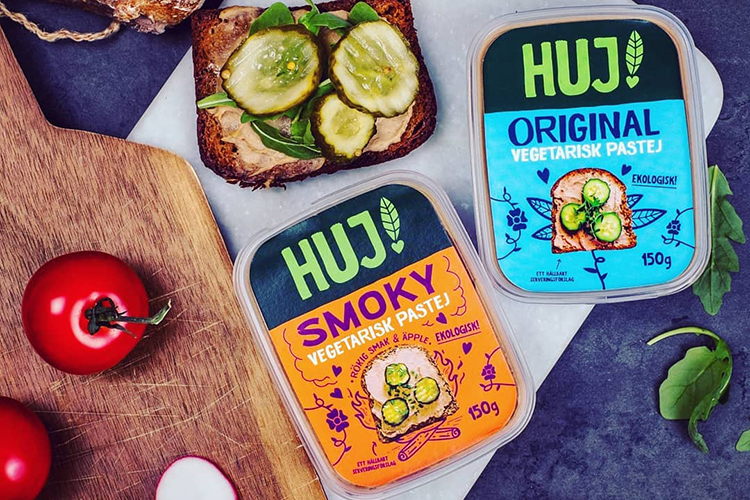 Två pastejförpackningar från HUJ! en smörgås med saltgurka vid sidan