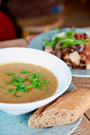 Vit skål med soppa i, toppad med färskt grönt. Ett bröd ligger vid sidan.