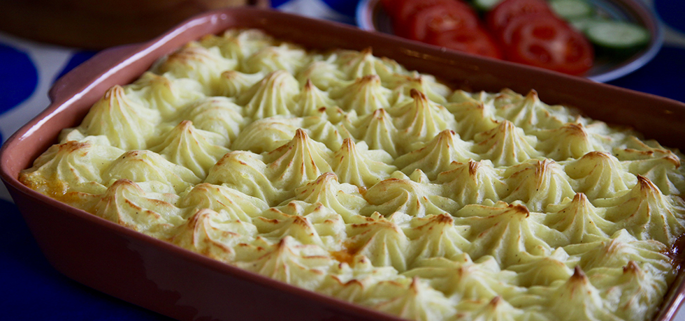 Rektangulär keramikform med spritsat mos, skivade tomat och gurka i bakgrunden