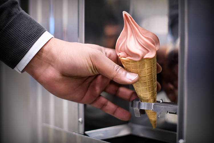 En hand tar en strut med rosa mjukglass från en mjukglassmaskin