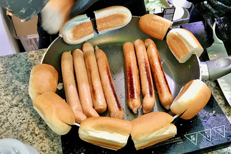 Stekpanna med varmkorv i, runtom korvbröd på kanten