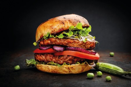 Burgare med grönsaker och sallad i bröd mot svart bakgrund. Ärtor bredvid