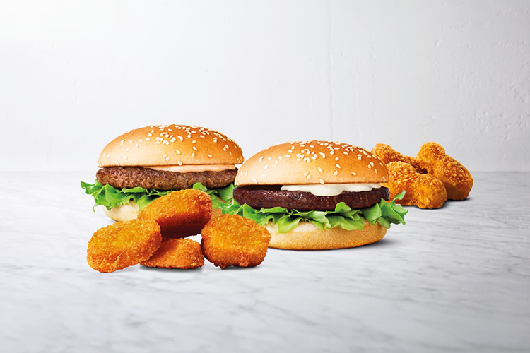 Två burgare med bröd och sallad, i för- och bakgrund nuggets