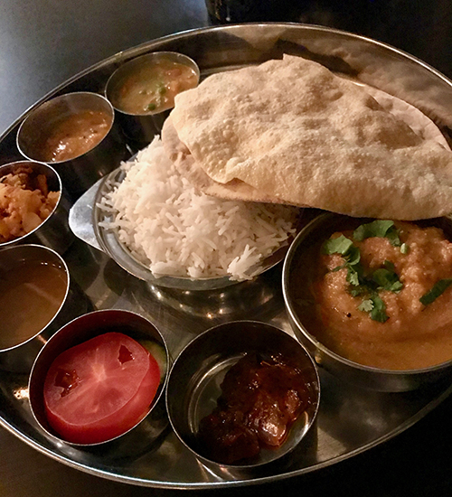 En rund silverbricka med små skålar med mat, i mitten ris och bröd