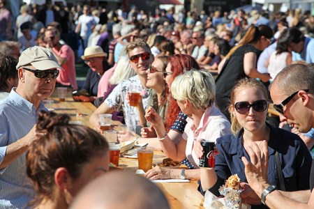En mängd personer sitter ute vid långbord och äter och dricker