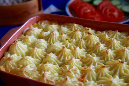 Rektangulär keramikform med spritsat mos, skivade tomat och gurka i bakgrunden