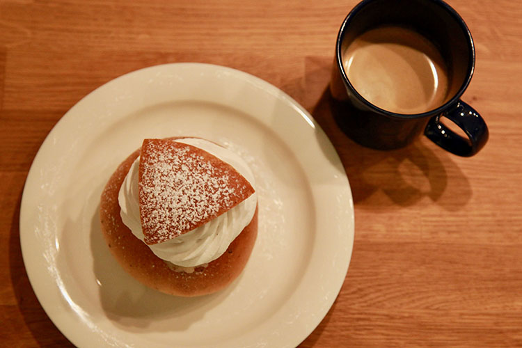 Semla på vitt fat, bredvid en kopp kaffe