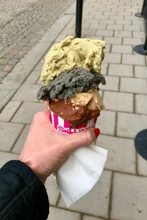 En hand håller en bägare med fyra glasskulor i. En liten plastsked nedstucken överst