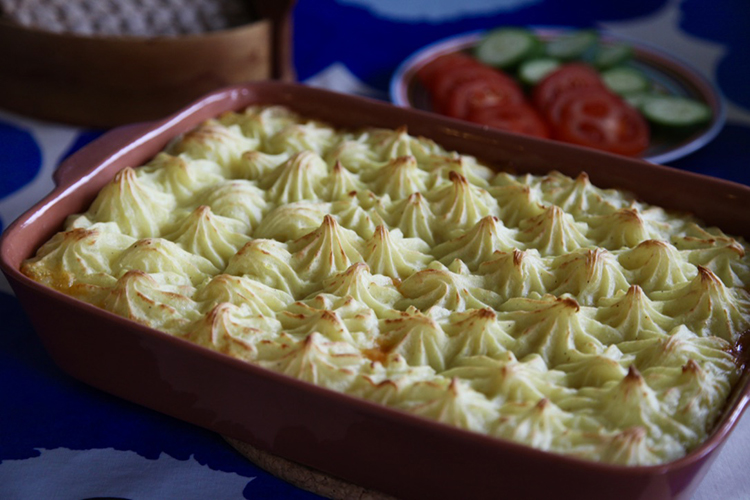 Rektangulär keramikform med spritsat mos, skivade tomat och gurka i bakgrunden