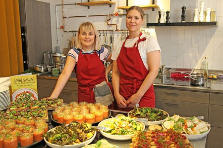 Två blonda kvinnor står vid ett buffébord