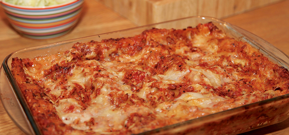 En ugnsform med lasagne, isbergssallad i skål i bakgrunden