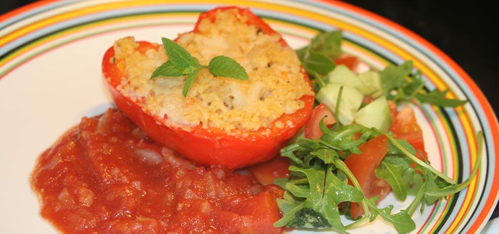 Fylld, röd paprika med smält ost ovanpå, på tallrik med tomatsås och salladsblad